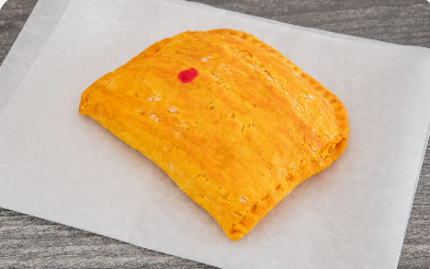 Golden Jamaican beef patty with flaky crimped crust on wax paper
