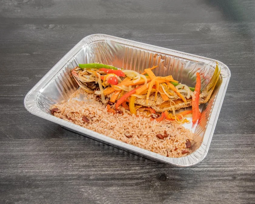 Whole escovitch fish topped with pickled vegetables and rice and peas served in a foil takeout tray
